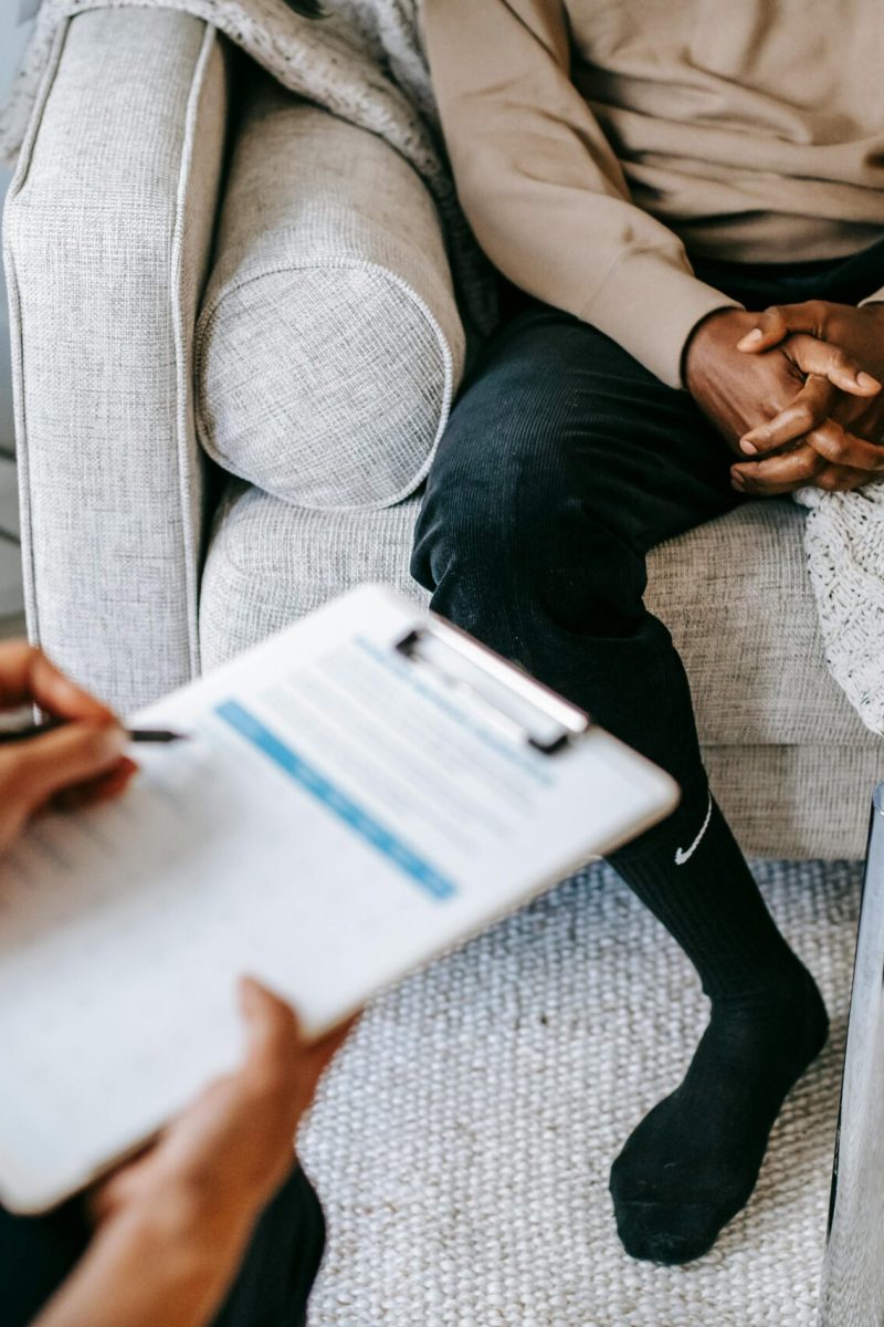 Therapist takes notes as client sits on a sofa during a psychotherapy session.
